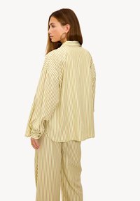 Camisa liviana a rayas en verde pálido y marrón. Presenta mangas largas, un corte relajado y dobladillo redondeado, acompañada de pantalones a juego.