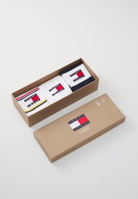 Set aus drei Paar Socken in einer braunen Kartonbox. Mit weißen, marineblauen und gestreiften Mustern, in denen die "TOMMY JEANS"-Logos deutlich sichtbar sind.