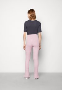 Um top ajustado cinza escuro com mangas curtas, combinado com calças flare de riscas em rosa claro. O conjunto possui uma silhueta elegante e uma textura suave.