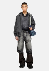 Veste à capuche grise sur une chemise coll bateau grise foncée, jeans gris déchirés avec des accents noirs, et un sac bandoulière bleu. Chaussures noires.