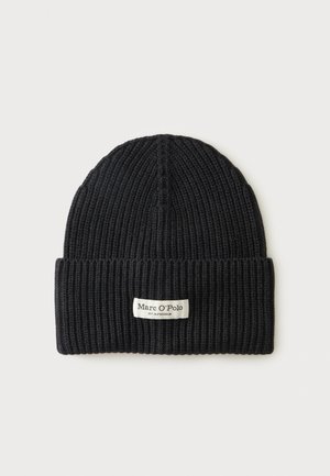 Bonnet en maille côtelée noire avec revers plié et une étiquette blanche rectangulaire portant la mention Marc O’Polo, posé sur un fond clair uni.