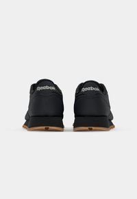 Sorte sportssko med en glatt overmateriale, minimalistisk design og gummisåle. Har Reebok-merke på hælen.