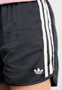 Black athletic shorts made of smooth, lightweight fabric, featuring three white vertical stripes and a small white logo detail.