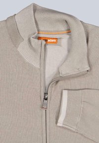 Hellgraue Zip-Up-Strickjacke mit einem hohen Kragen, gerippten Bündchen, strukturiertem Stoff und einem orangen Etikett im Kragen. Verfügt über eine Seitentasche.