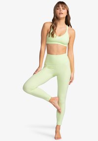 Lichtgroene sportbeha en bijpassende legging van rekbaar, glad materiaal. De leggings hebben een hoge tailleband en een aansluitende pasvorm.