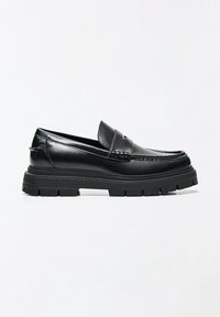 Mocassin en cuir noir avec semelle épaisse crantée et couture style mocassin sur fond blanc.