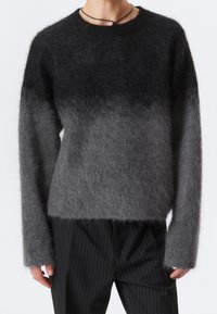 Pull en ombre gris en fils moelleux, avec des manches longues et un col rond. Porté avec un pantalon à rayures. Texture douce et coupe ample.