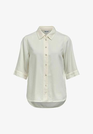 Chemise à manches courtes de couleur crème avec col pointu et ourlet arrondi, comportant sept boutons visibles sur le devant.