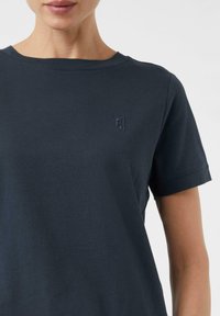 Granatowa bawełniana koszulka z krótkim rękawem, okrągłym dekoltem i subtelnym logo na piersi. Gładka tekstura, minimalistyczny design.