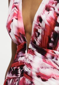 Prim-plan al unei rochii cu decolteu adânc în V, având un model abstract în nuanțe de roșu, roz și alb și detalii cu țesătură adunată în zona taliei.
