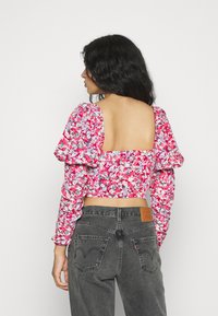 Top de flores em rosa com mangas longas bufantes e um design de costas quadradas, combinado com jeans cinzentos de cintura alta com bolsos traseiros.