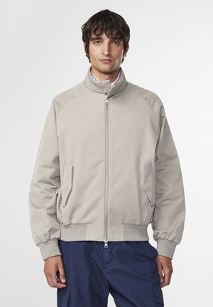 Lys beige bomberjakke med høj krave, frontlynlås og sidelommer. Har ribbede manchetter og kant. Glat stoftekstur.