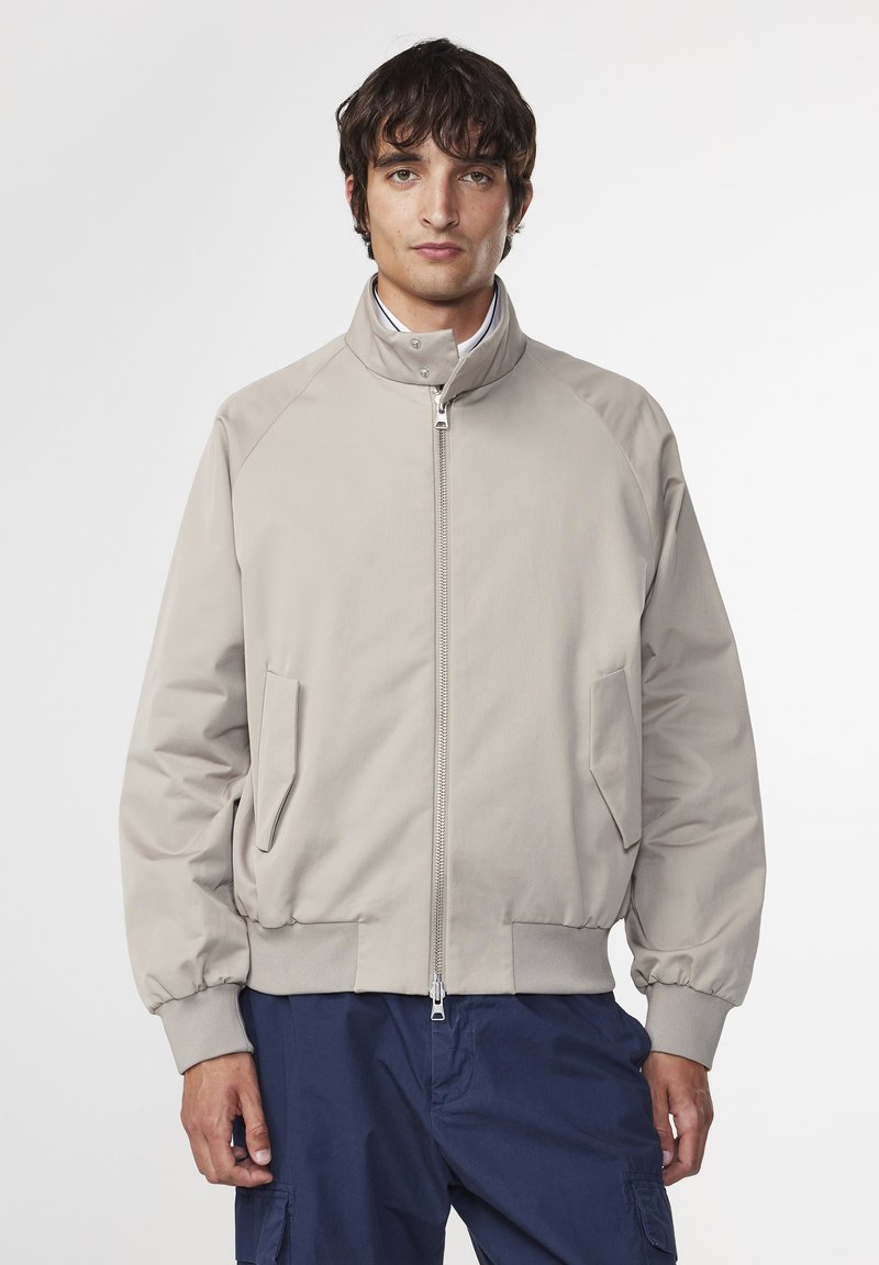 Giacca bomber beige chiaro con colletto alto, chiusura frontale con zip e tasche laterali. Presenta polsini e orlo a coste. Tessuto dalla consistenza liscia.