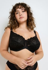 Bralette in pizzo nero con motivi floreali, fascia solida, spalline regolabili e chiusura a gancio sul davanti, con sottostrato liscio.