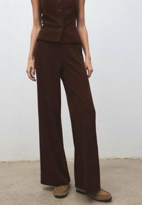 Brown, textured sleeveless top with buttons, paired with wide-leg brown pants. Outfit features a structured silhouette and soft fabric.