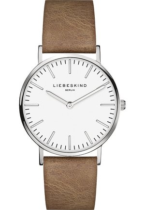 Montre ronde avec un cadran blanc, un boîtier en argent et un bracelet en cuir marron. Présente des index horaires minimalistes et un logo de marque subtil.