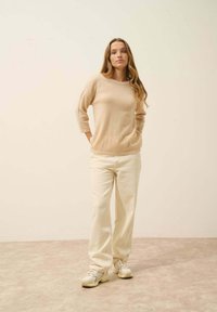 Beige pletený svetr s tříčtvrtečními rukávy, spárovaný s bílými širokými kalhotami a světle barevnými teniskami. Měkké materiály, jednoduchý design.