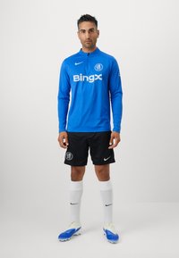 Blå langærmet sportshem med "Bingx" logo, sorte shorts med klubemblemet, hvide strømper og blå støvler med gule accenter.