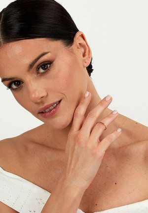Gouden ring die op een vinger rust, met een verfijnd ontwerp. De drager heeft een egale teint en een neutrale nagellak kleur.
