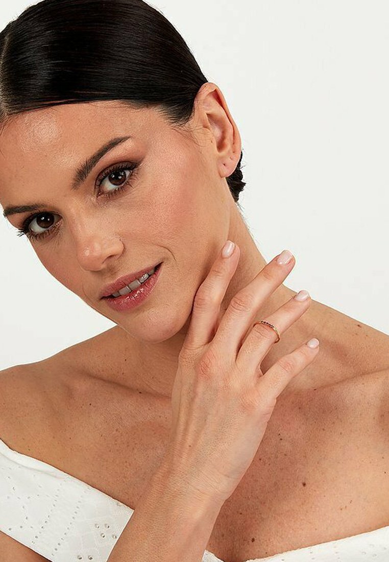 Guldtonad ring som vilar på ett finger, med en delikat design. Bäraren har en jämn hy och en neutral nagelfärg.