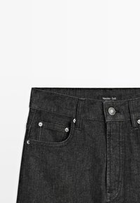 Area della vita di jeans in denim nero con tasche frontali, passanti per cintura, un bottone in metallo e un'etichetta del marchio Massimo Dutti ben visibile.