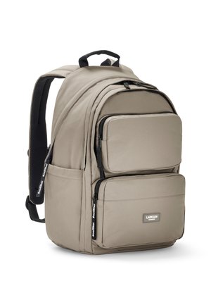 Zaino beige con una finitura in tessuto morbido, multiple tasche con cerniera, spallacci imbottiti e una maniglia superiore per il trasporto.