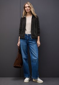 Donkergrijze ritssluiting-jasje, beige top, blauwe wijde jeans, witte sneakers en een bruine schoudertas. Soepele jastextuur, casual pasvorm.