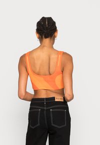 Top laranja cropped com um design texturizado e padrão, com alças largas, combinado com jeans pretos com costura branca e um rótulo.