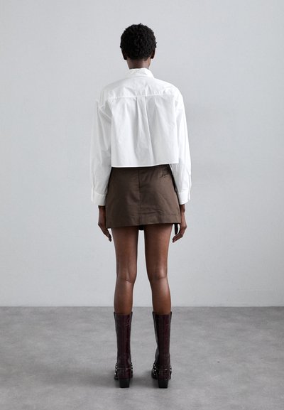 Chemise blanche coupée, mini jupe marron, bottes bordeaux jusqu'aux genoux. Tissu lisse, design structuré, lignes simples, sans motifs ni accents visibles.