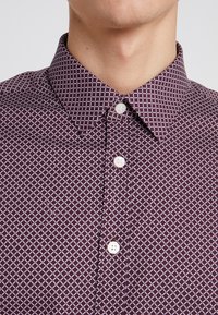 Camicia button-up bordò con un motivo geometrico a diamante bianco, colletto a punta e bottoni simili a perle. Tessuto morbido al tatto.