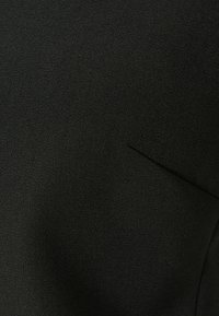 Tessuto nero con una superficie liscia, caratterizzato da una piccola tasca a filetto. Il materiale sembra leggero e morbido.