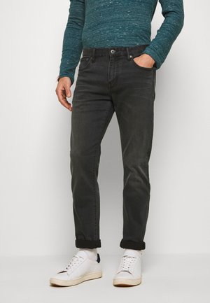 Jeans de denim gris oscuro con corte ajustado, bolsillos frontales y puños enrollados. Combinados con zapatillas blancas y una camisa de manga larga texturizada azul.