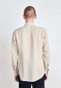 Camicia a maniche lunghe in lino beige con vestibilità rilassata, colletto stretto, polsini con bottone e texture sottile, caratterizzata da un orlo curvo sul retro.