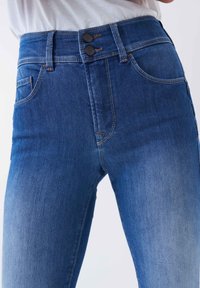 Jeans de mezclilla azul de cintura alta con un acabado desgastado, que cuentan con dos cierres de botón, bolsillos cosidos y un detalle minimalista.