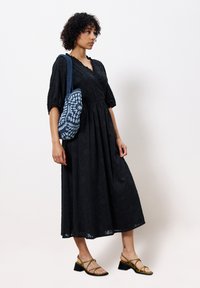 Schwarzes Midikleid mit strukturiertem Blumenmuster, Puffärmeln und V-Ausschnitt; kombiniert mit einer blauen gemusterten Tasche und olivgrünen Sandalen mit Riemchen.