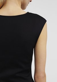 Haut noir sans manches avec un col rond, texture lisse, coupe ajustée et coutures nettes visibles aux épaules.