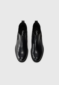 Bottes chelsea en cuir noir avec une finition lisse, panneaux latéraux élastiques et une tirette à l'arrière. Présentent un bout rond et une semelle fine.