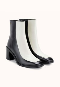 Bottines en cuir noir et blanc, avec un talon épais, une texture lisse, des panneaux contrastants et une fermeture éclair.