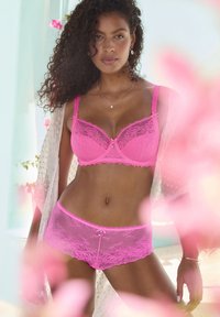 Pink lace lingerie set featuring a balconette bra with scalloped edges and decorative bow, paired with matching boyshorts.