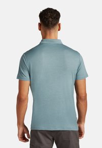 Kortärmad polo i ljusblått, tillverkad av textil med struktur, med en vikbar krage och rak fåll. Inga synliga logotyper eller mönster.
