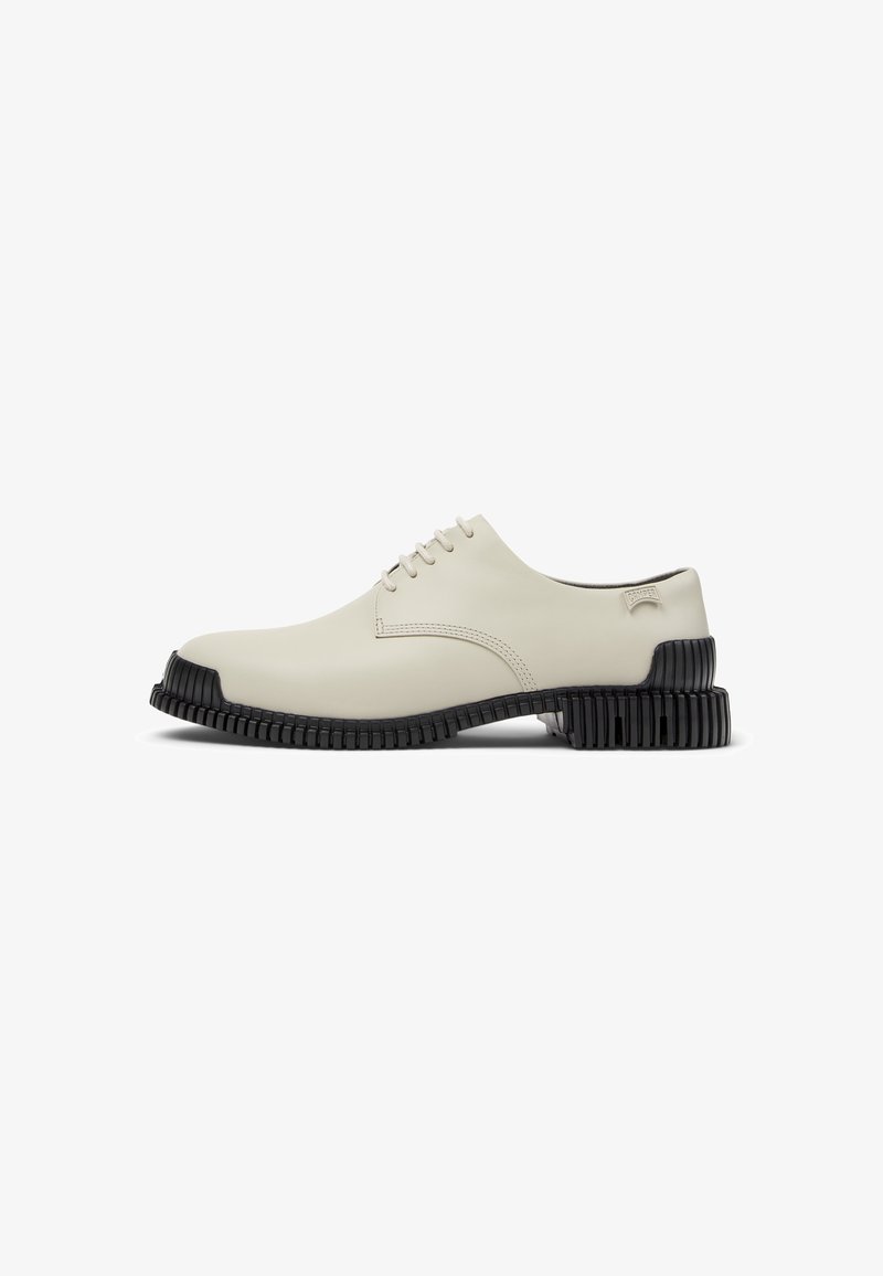 Cream-colored lace-up shoe with a textured black sole, featuring a sleek design and minimalistic style. Side view against a white background.