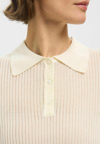 Pull polo en crème tricoté avec une texture côtelée, doté d'un col, d'un avant à quatre boutons et d'un subtil éclat.