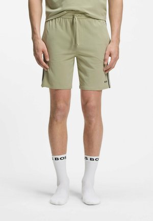 Mand iført lysegrønne shorts med snor og hvide sokker med sort "BOSS" tekst, stående mod en ensfarvet hvid baggrund.