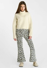 Lichtbeige, fluffy coltrui gecombineerd met wijde, dierenprint broek in wit en grijs, met een luipaardpatroon.