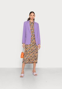 Blazer lavanda sobre um vestido floral preto com destaques em laranja e amarelo. Acompanhado de sandálias de salto lavanda e uma bolsa laranja.