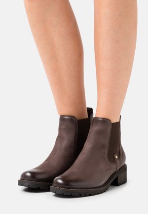 Bottes basses en cuir marron à finition lisse, avec des panneaux latéraux élastiques et un petit talon bloc, ornées de coutures discrètes et d'accents métalliques.