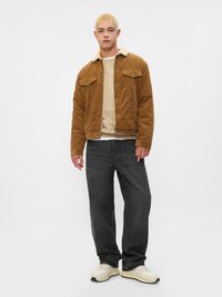Brun kordfløyelsjakke med en beige faux fur-krage, sammen med mørke jeans og kremfargede sneakers, mot en ensfarget bakgrunn.
