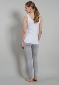 Canotta bianca e leggings grigi in cotone morbido, dal design aderente. La canotta presenta spalline larghe; i leggings sono alla caviglia con una trama liscia.