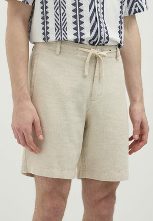 Pantaloni corti in lino color beige chiaro con vita regolabile, dotati di tasche laterali e sottili accenti testurizzati.