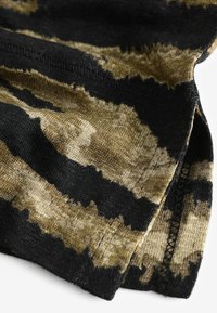 Gros plan d'un tissu avec un motif tie-dye noir et marron montrant des coutures détaillées et un ourlet sur un matériau en maille douce.
